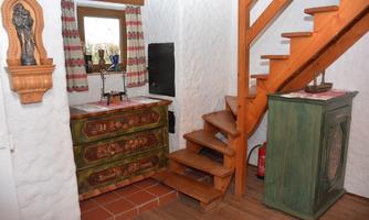 A cozy interior with a decorated dresser and a wooden staircase. The window lets in light and the walls are designed in a warm white.