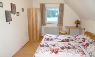 A beautiful bedroom with a double bed and colorful bedding. There is a desk and a wardrobe, as well as a window with a view of nature.