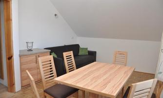 A modern room with a wooden table and chairs. In the background, there is a couch and a chest of drawers.