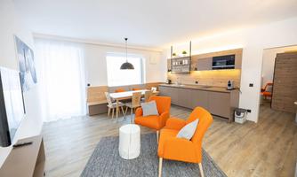 A modern living room with orange armchairs and a dining table. The bright kitchen with wood elements gives the room a cozy atmosphere.