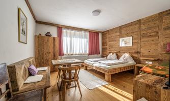 A cozy room with wooden furniture and two beds. Large windows provide plenty of natural light and an inviting atmosphere.