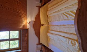 A cozy bedroom with a large bed and yellow blankets. Next to the bed are nightstands with lamps and a window that lets in light.