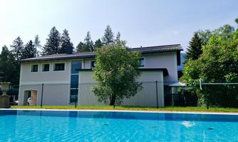 A modern house with a clear pool and beautiful trees in the garden. The surroundings are calm and green.