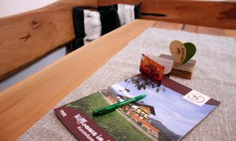 A table with an inviting brochure and a green pen. In the background, cushions and a cozy wooden bench can be seen.