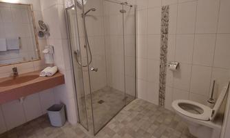 A modern bathroom with a large glass shower and a toilet. The walls are tiled in light colors and there is a mirror above the sink.