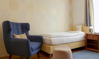 A cozy room with a single bed and a blue armchair. The walls are light, and the room is neat and inviting.