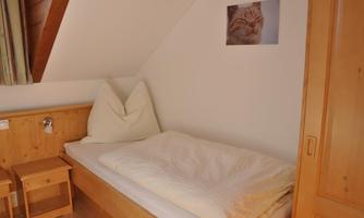 A cozy bedroom with a single bed and wooden-paneled walls. A picture of a cat hangs on the wall.