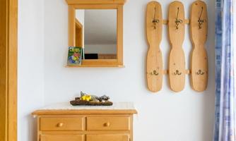A cozy entrance area with a wooden sideboard and a wall mirror. Several wooden items are hanging on the wall, arranged decoratively.