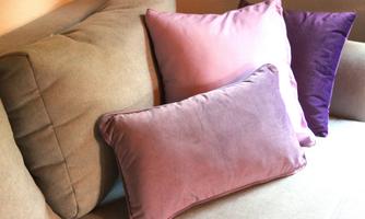 A cozy sofa with several cushions in various shades of purple and pink. The cushions give the room an inviting atmosphere.