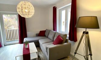 A modern living room with a gray sofa and red cushions. There are large windows and a stylish floor lamp.