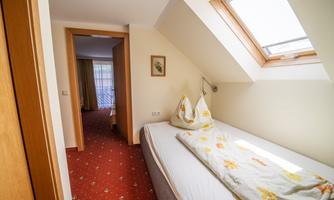 A bright room with two beds and a skylight. The floor is carpeted, and through an open door, another room is visible.