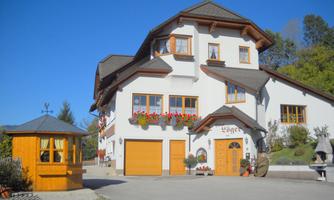 A lovely two-story house with flower boxes and two garage doors. In the foreground, there is a small wooden gazebo.