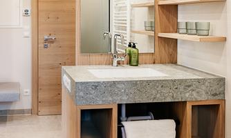A modern bathroom with a beautiful sink made of stone and wood. On the wall, shelves with bathroom utensils and a large mirror are visible.