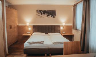 A modern bedroom with a double bed and hardwood floor. Soft lighting and a window create a cozy atmosphere.