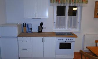 A bright kitchen with modern white cabinets and a wooden countertop. On the countertop are a kettle, a coffee machine, and various cooking appliances.