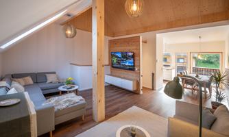 A modern living room with a cozy couch and a television on the wall. The room is well-lit and offers a beautiful view of nature outside.