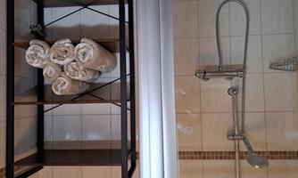 A modern shower cubicle with a handheld shower and bright tiles. Next to the shower stands a shelf with neatly stacked towels.