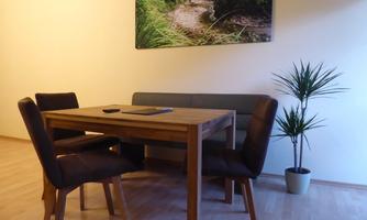 A simple dining room with a wooden table and four chairs. A picture of a green landscape hangs on the wall.