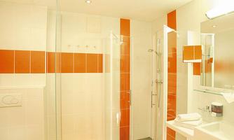 A modern bathroom with a glass shower and orange accents. There is also a sink and a large mirror.