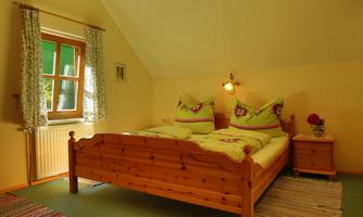 A cozy bedroom with two beds and colorful pillows. The room is bright and friendly with wooden details and a window that lets in plenty of light.