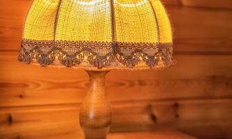 A pretty table lamp with a beige-colored lampshade stands on a round table. Next to it lies a wooden heart on a decorative base.
