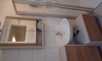 A modern bathroom with a shower, a sink, and a mirror. The walls are brightly tiled, and there are wooden shelves for storage.