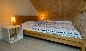 A cozy bedroom with a double bed and a bedside table. The wooden ceiling and soft lighting create a warm atmosphere.