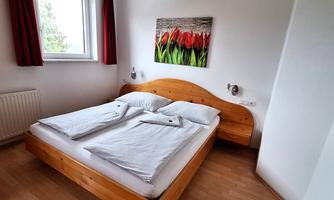 A bright bedroom with a double bed and fresh white bed linens. A picture of colorful tulips hangs on the wall and the window lets in daylight.