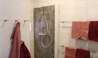 A modern bathroom with a shower and elegant tiles. Towels in various shades of red are hanging on the walls.