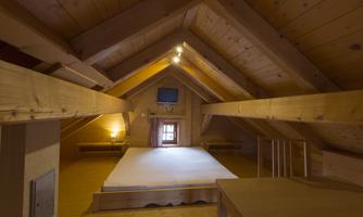 A cozy, wood-paneled attic room with a bed and a small table. A television and a window provide light and comfort.