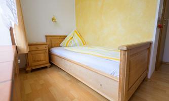 A cozy bedroom with a light wooden bed and a bedside lamp. The walls are painted yellow and there are wood-colored furniture.