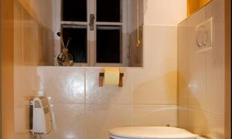 A clean bathroom with a toilet, a window, and a wooden ceiling. The walls are light tiled and there is a towel rack.
