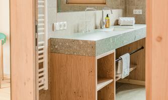 A modern bathroom with a wood and stone surface. There is a large mirror and a window view.