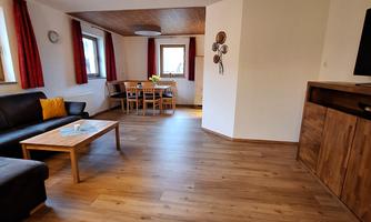 A bright living space with wooden flooring and large windows. A cozy seating area and a dining table are available.