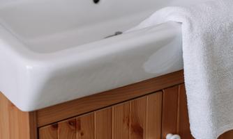A simple sink with a wooden cabinet. A towel lies on the edge of the basin.