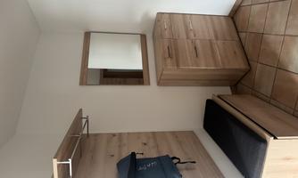 A modern hallway with a wooden wardrobe and a bench. A mirror and a bag hang on the wall.