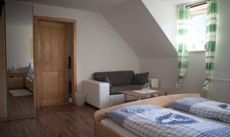 A bright room with two beds, a couch, and a table. Large windows with striped curtains let in a lot of light.