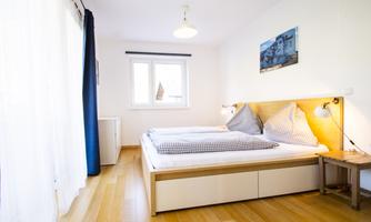 A bright bedroom with two beds and checked bed linens. Large windows provide plenty of daylight and a cozy atmosphere.