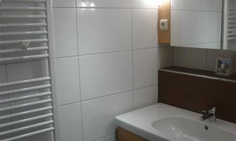 A modern bathroom with white tiles and a wooden washbasin. A towel warmer is mounted on the wall, and a mirror is placed above the sink.