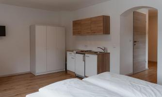A modern room with a small kitchen and a bedroom. The floor is made of wood, and the walls are painted in neutral colors.