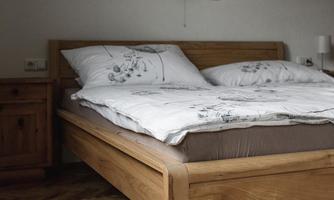 A cozy bedroom with a wooden bed and beige-brown bedding. The wooden floor creates a warm atmosphere.