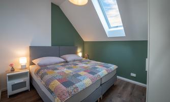 A cozy bedroom with a large bed and colorful bedding. A skylight provides plenty of daylight.