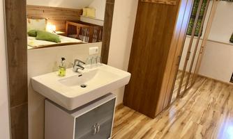 A modern room with a sink and a wooden cabinet. The floor is made of light laminate and the walls are neutrally designed.