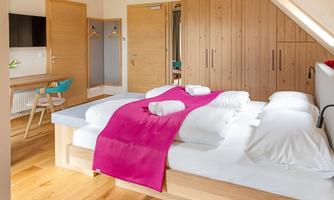 A modern bedroom with a large bed and bright wooden furniture. The walls are painted in natural tones, and there is a small workspace.