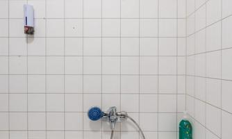A white bathtub in front of a tiled wall. A blue faucet and some bottles can be seen on the tub.