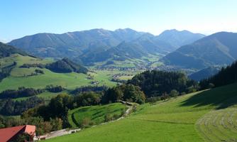 A beautiful mountain landscape with green meadows and gentle hills. In the background, majestic mountains and a blue sky can be seen.