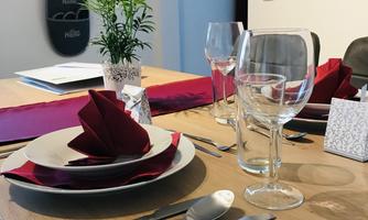 A beautifully set table with red napkins, dishes, and glasses. In the background, there is a plant and decorative wall design.