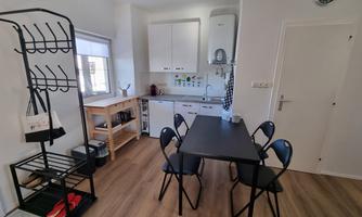 A bright kitchen with modern furniture and a table for four people. On the side, there is a rack for hanging jackets and bags.
