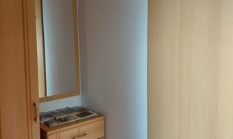 A small entrance area with a wooden cabinet and a mirror. Hooks for coats and bags are hanging on the wall.