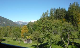 An idyllic landscape with lush greenery and trees. In the background, the snow-capped mountains are visible.